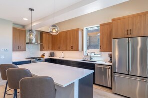 A modern kitchen with wooden cabinets, stainless steel appliances, and a central island with bar stools. - 224 Frisco Alley Unit E By Summit County Mountain Retreats (Frisco)