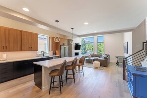 A modern kitchen with a large island, wooden cabinets, and a dining area with a sofa and table. - 224 Frisco Alley Unit E By Summit County Mountain Retreats (Frisco)