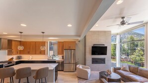 A modern kitchen with wooden cabinets, a central island, stainless steel appliances, pendant lighting, and a large window offering a mountain view. - 224 Frisco Alley Unit E By Summit County Mountain Retreats (Frisco)