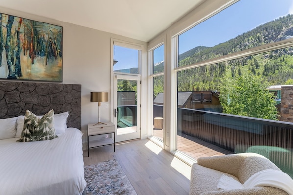 A bedroom with a large window, a bed, a nightstand, and a painting. - 224 Frisco Alley Unit E By Summit County Mountain Retreats (Frisco)