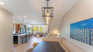 A modern kitchen with a central island, a dining area with a long table, and a living space with a sofa and a painting. - 224 Frisco Alley Unit E By Summit County Mountain Retreats (Frisco)