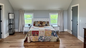 A bedroom with a large bed, two bedside tables, a nightstand, a tall floor lamp, and a window with curtains. - Spacious loft style apartment with gorgeous view (Watertown)