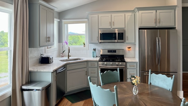A modern kitchen with grey cabinets, stainless steel appliances, a dining table with chairs, and a window with a view of greenery. - Spacious loft style apartment with gorgeous view (Watertown)