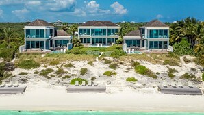 A beachfront property with three modern villas, each with large glass windows and a flat roof. - Beachfront Villa w/ Private Pool & Concierge – Villa Helios (Long Bay Beach)