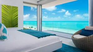 A bedroom with a large window offering a view of the ocean and beach. - Beachfront Villa w/ Private Pool & Concierge – Villa Helios (Long Bay Beach)