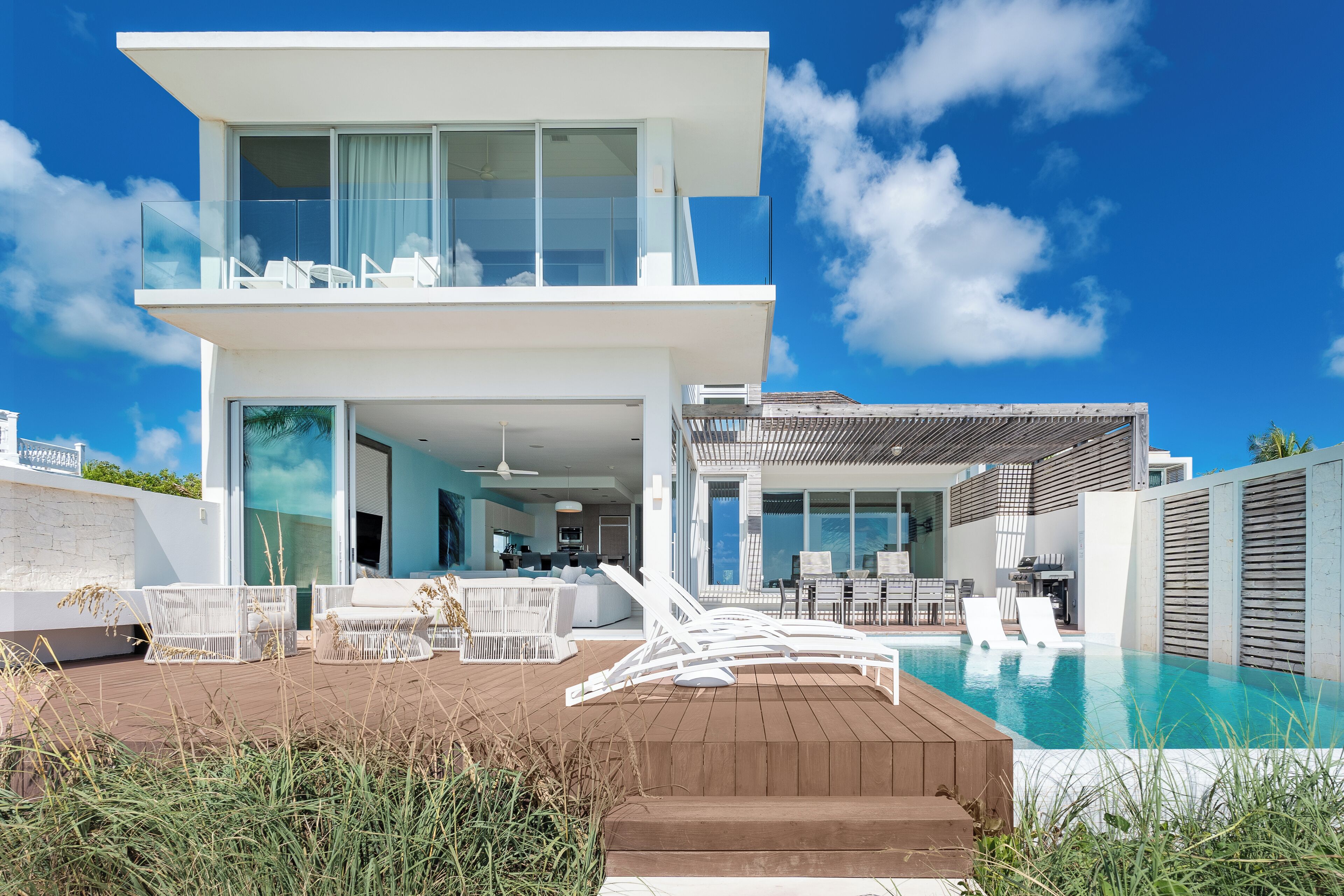 Ein modernes, zweistöckiges Haus mit Pool, Sitzgelegenheiten im Freien und einem Balkon.
