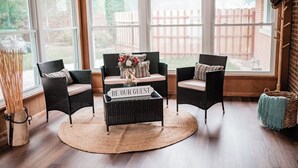 A cozy seating area with wicker furniture, a round rug, and a sign that reads "BE OUR GUEST".