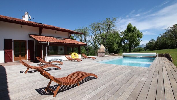 A wooden deck with lounge chairs, a swimming pool, and a house with a tiled roof. - Arlotia - Ascarat - Gîte (ASCARAT)