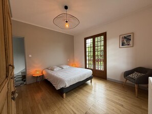 A bedroom with a bed, a wooden floor, a door with a view, and a chair. - Arlotia - Ascarat - Gîte (ASCARAT)