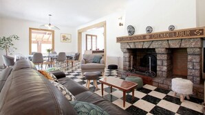 A living room with a checkered floor, a fireplace, and a dining area with chairs and a table. - Arlotia - Ascarat - Gîte (ASCARAT)