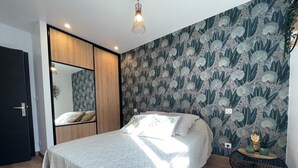 Un dormitorio con cama, armario de madera, espejo y pared con estampado floral.