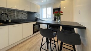 Una cocina moderna con armarios blancos, encimera negra y un taburete negro.