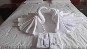 A hotel bed with white linens and towels arranged in the shape of two swans. - HOTEL BURJ KHALIFA (Santa Ana)