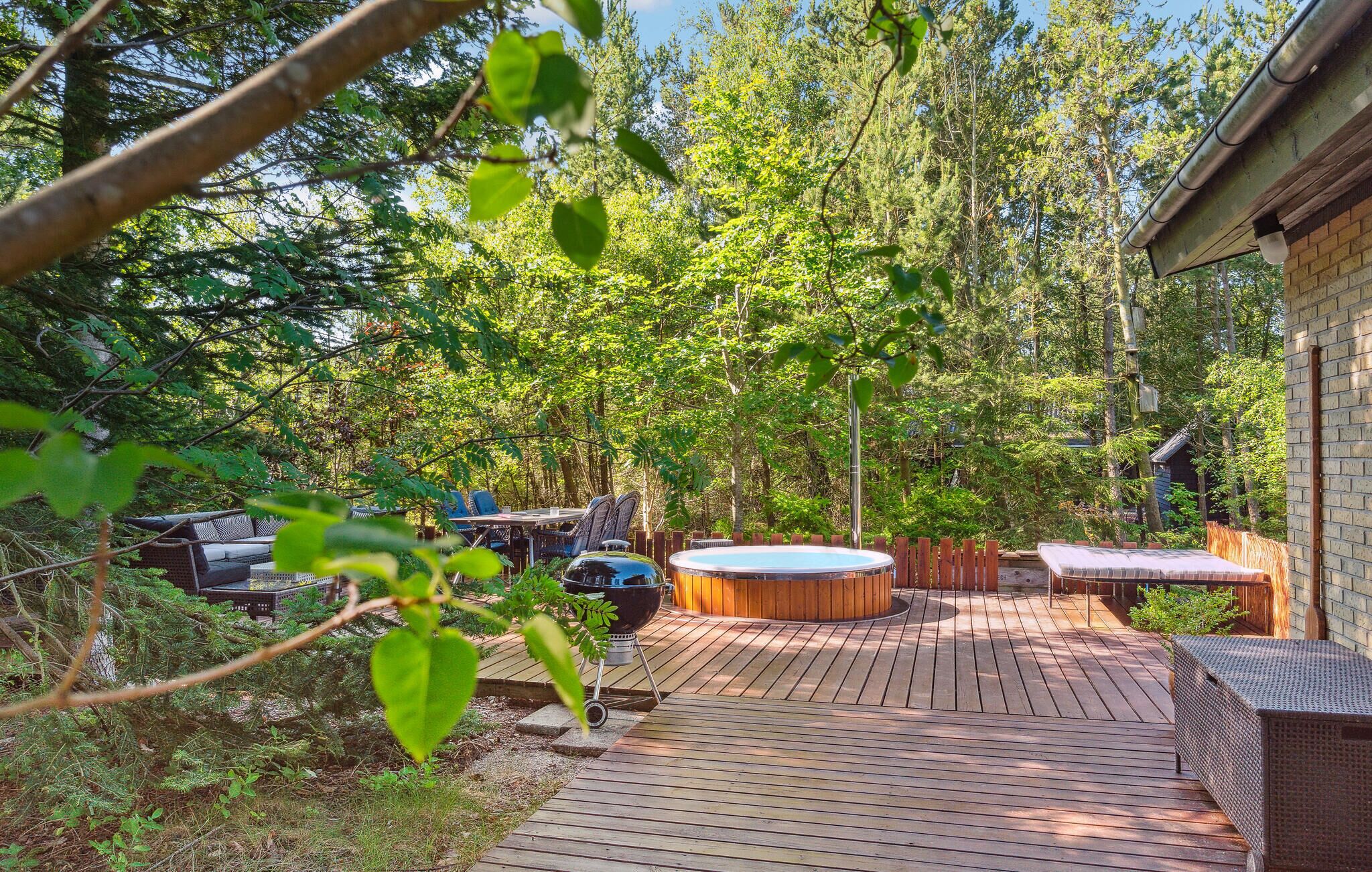 A wooden deck with a hot tub, outdoor furniture, and a brick building in the background.