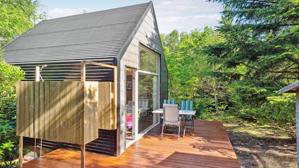 Una casa moderna con terraza de madera, puerta de cristal que da a un patio y un pequeño espacio exterior con mobiliario.