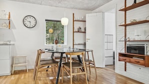 Un comedor con una mesa redonda, cuatro sillas de madera, un reloj de pared y una ventana con vistas a zonas verdes.