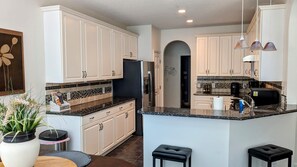 A modern kitchen with white cabinets, a granite countertop, and a central island with stools.