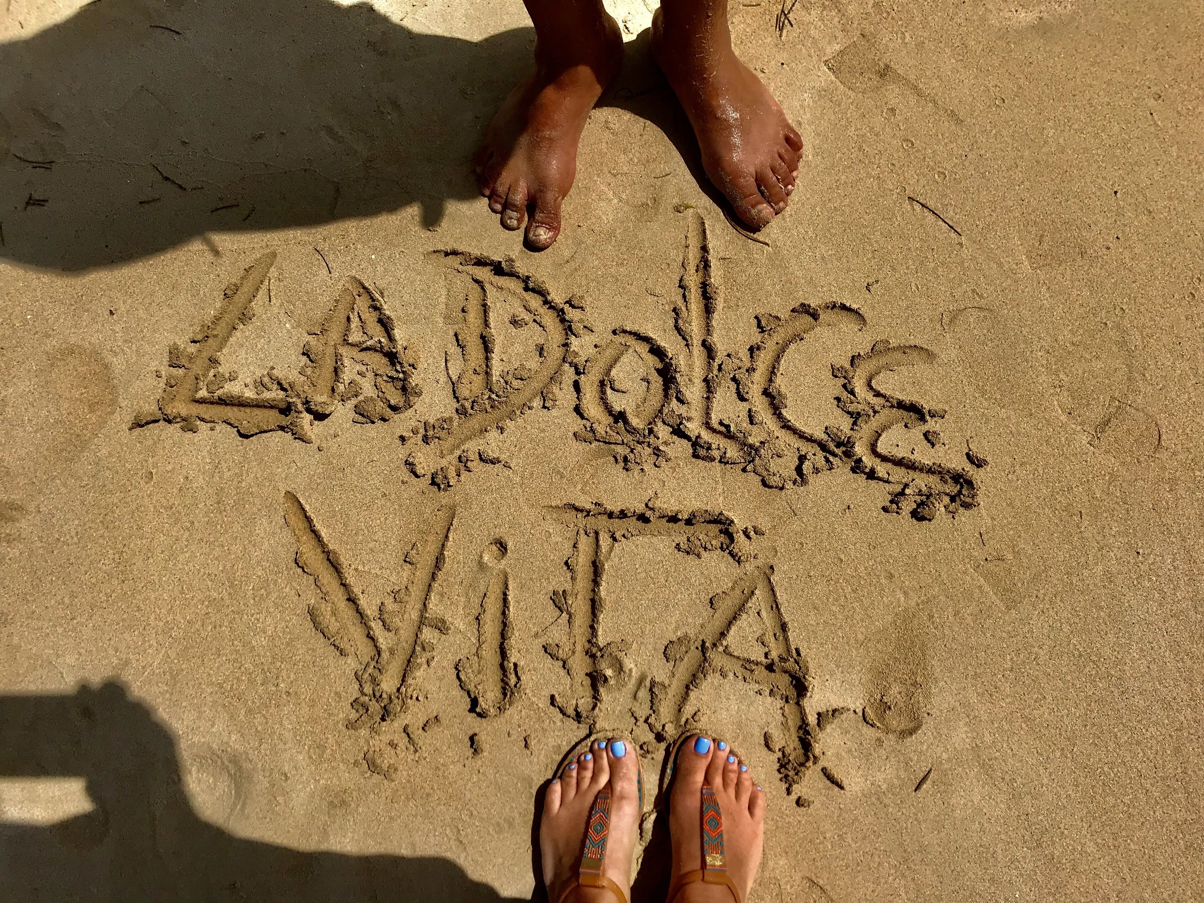 A sandy beach with footprints and the words "LA DOLCE VITA" written in the sand.
