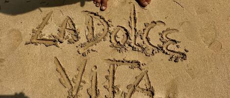 A sandy beach with footprints and the words "LA DOLCE VITA" written in the sand.