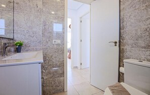 Une salle de bain avec un lavabo, un miroir et des toilettes. Une porte donne accès à une autre pièce.