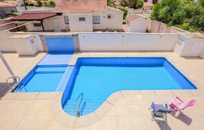 Une piscine rectangulaire dotée d’un plongeoir et de deux chaises longues.