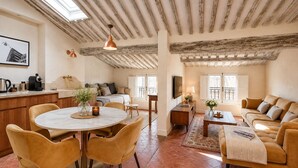 A spacious living area with a high ceiling, a dining table with chairs, a sofa set, and a kitchen area with a coffee machine.