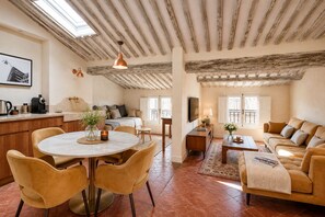 A spacious living area with a high ceiling, a dining table with chairs, a sofa set, and a kitchen area with a coffee machine.