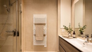A modern bathroom with a glass shower enclosure, a towel rack, a vanity with a mirror, and a plant.