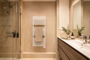A modern bathroom with a glass shower enclosure, a towel rack, a vanity with a mirror, and a plant.