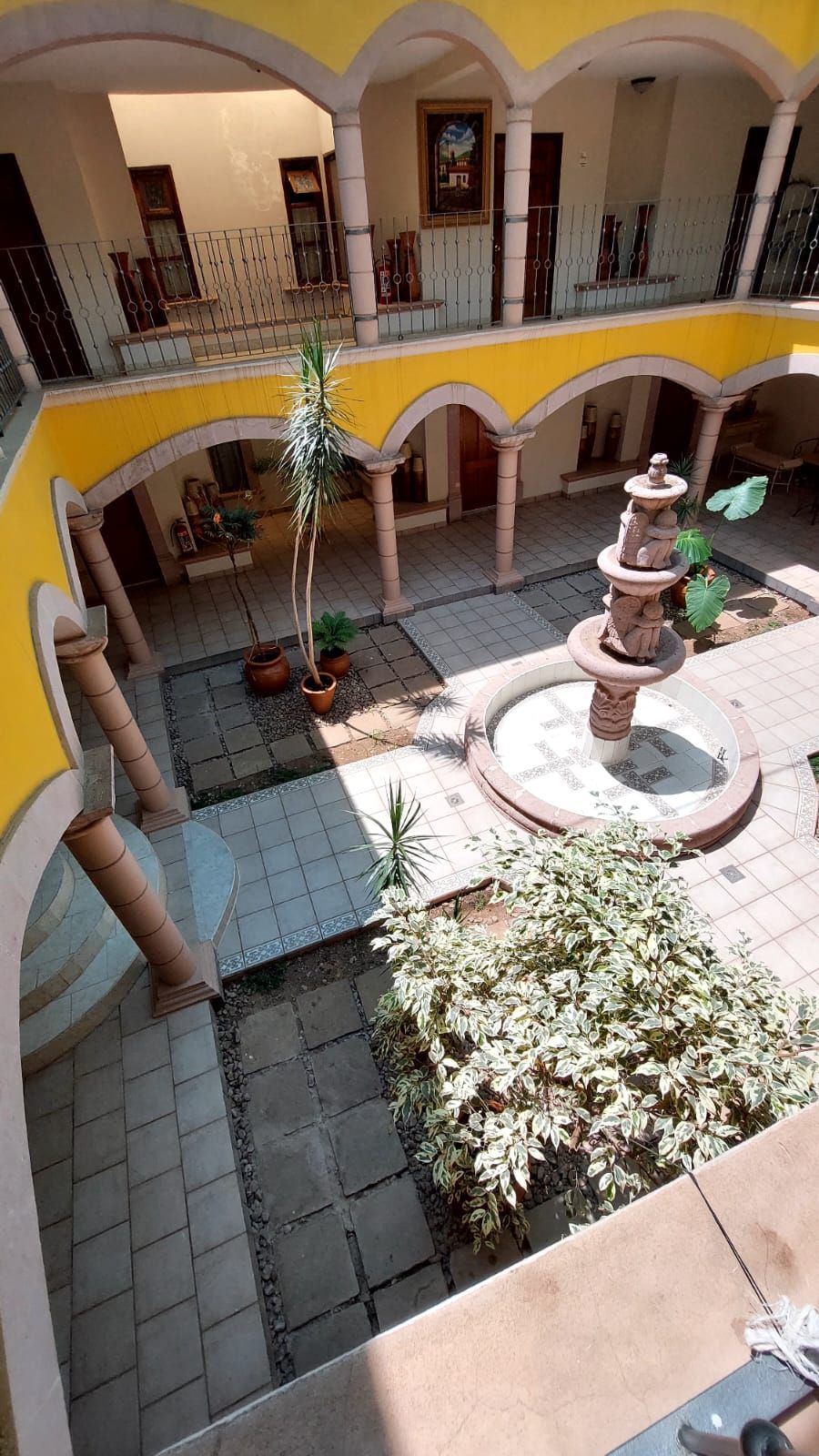 A courtyard with a central fountain, potted plants, and a tiled floor.