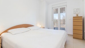Een slaapkamer met een bed, een houten dressoir en een raam met uitzicht op bomen.