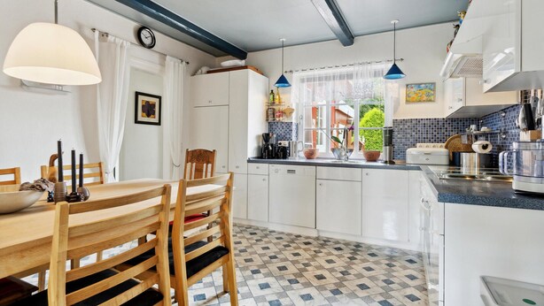 Eine moderne Küche mit weißen Schränken, einer gefliesten Spritzschutzwand und einem Essbereich mit Holztischen und einem Tisch.
