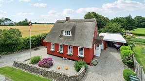Ein rotes Haus mit einem Strohdach, einer Schotterauffahrt und einer Fahnenstange.