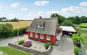 Une maison rouge avec un toit de chaume, une allée gravillonnée et un mât pour drapeau.