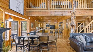 A wooden cabin interior with a dining area, kitchen, and a black leather couch. - Gorgeous Unique, Rustic Cabin on Arapaho! 2 Kings, Loft Area with a Full, and a Bunk Room! (Duck Creek Village)