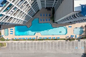 Vista aérea de un hotel con una gran piscina central, múltiples balcones y un estacionamiento.