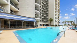 Zona de piscina amb diverses piscines, gandules i un edifici amb balcons.