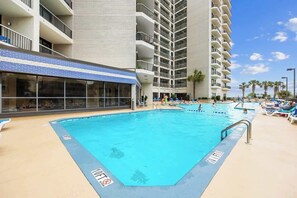A pool area with multiple swimming pools, lounge chairs, and a building with balconies.