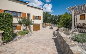 A modern two-story house with a paved driveway leading to a stone-walled patio area. - Awesome home in Rakotule (Rakotule)