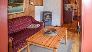 A cozy room with a red patterned sofa, a wooden table with a bowl, a stone fireplace, and a kitchen visible through an open door. - Nice home in Rauland with kitchen (Rauland)