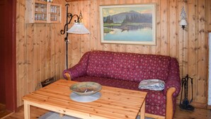 A cozy room with a wooden floor, a red patterned sofa, a wooden table with a bowl, a lamp, and a painting of a landscape. - Nice home in Rauland with kitchen (Rauland)