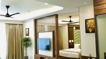 A modern hotel room with a flat-screen TV, a bed with a patterned bedspread, a green sofa, a small refrigerator, and a ceiling fan.