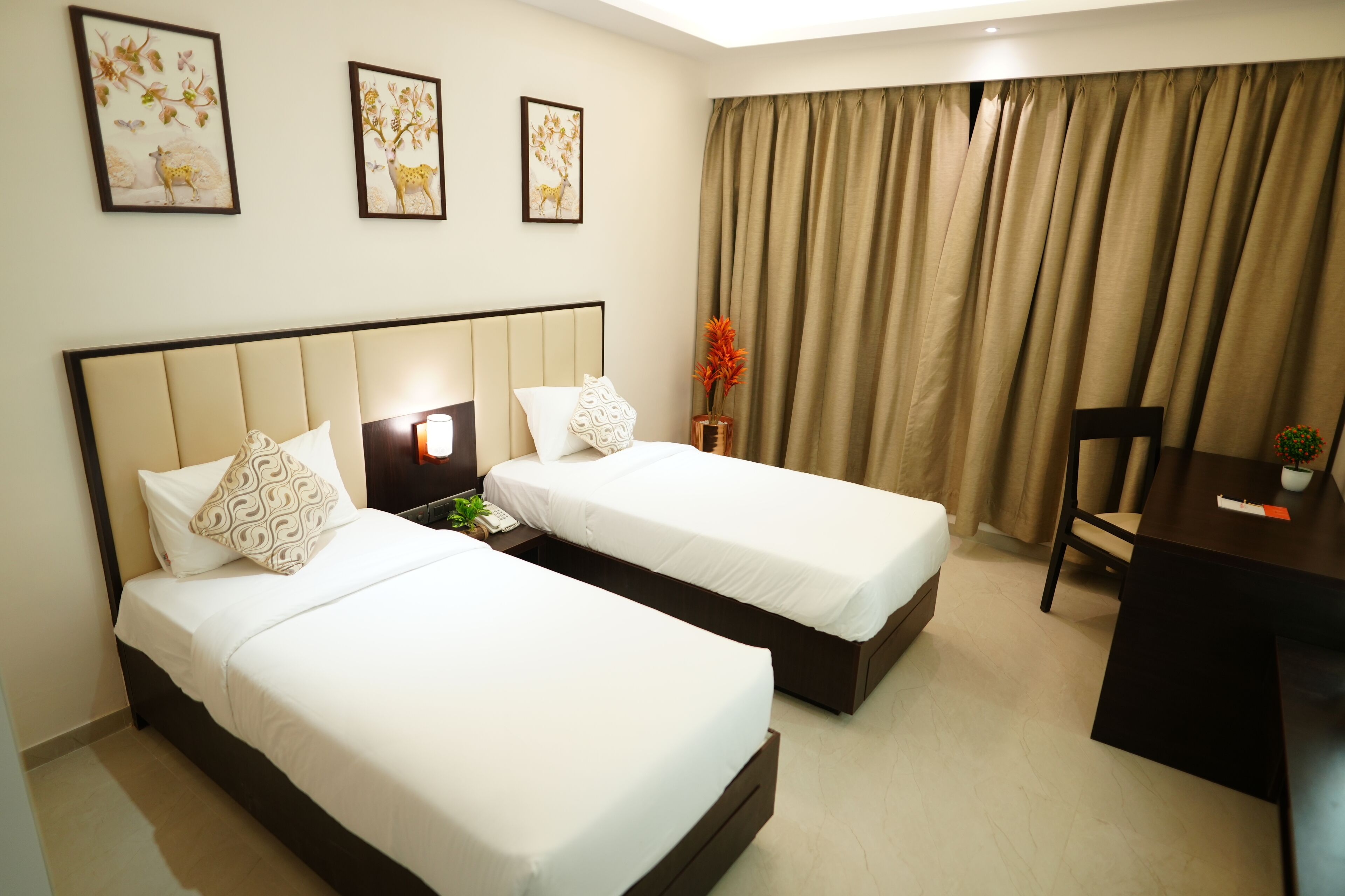 A hotel room with two single beds, a desk, a chair, and a large window with curtains.