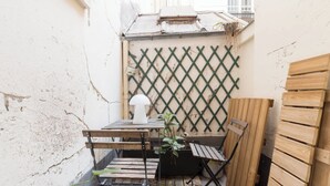 Un petit espace extérieur aménagé avec une table et des chaises, une plante en pot et un banc en bois.