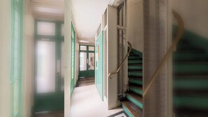 Un couloir avec des portes vertes, un escalier avec des rampes en métal et un sol à motifs.