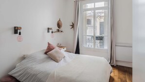 Une chambre à coucher avec un lit, une table de chevet, une fenêtre avec des rideaux et une vue sur l’extérieur.