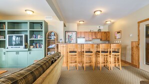 A compact living space with a kitchenette, a sofa, a TV, and a bookshelf. - Perfect Creekside Studio that Opens Right onto the Skiway!  (Silver Star Mountain)