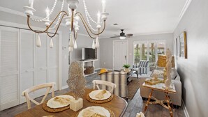 A dining area with a chandelier, a dining table set with plates and a centerpiece, and a sofa in the background.