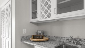 A kitchen with white cabinetry, a granite countertop, a stainless steel sink, and a wine sign.