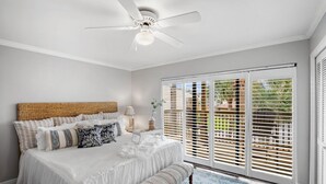 A bedroom with a large bed, a ceiling fan, and a view through sliding glass doors.